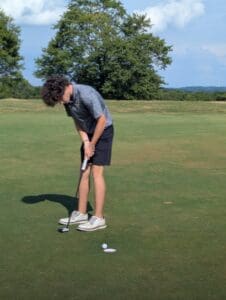 Golfer putting on green under clear sky with trees in background.