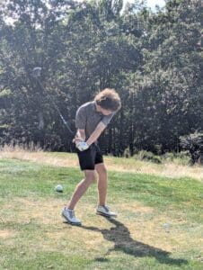 Golfer in mid-swing on a sunny day at a lush golf course, surrounded by trees.
