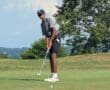 Teen golfer putting on a sunny day at the golf course, surrounded by trees and a clear sky.