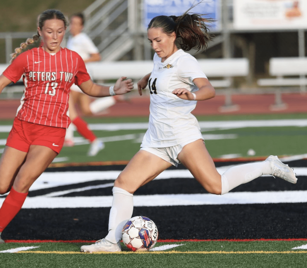Soccer players in white and red jerseys compete for the ball during a match on a green field.