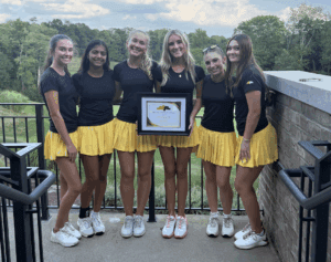 Group of young women in matching outfits holding a first place certificate on a terrace with a scenic backdrop.