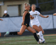 Two female soccer players compete for the ball during a match on a field.