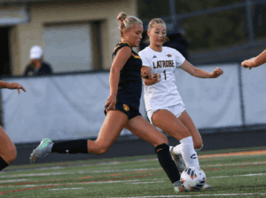 Two female soccer players compete for the ball during a match on a field.