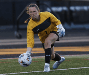 Goalkeeper in yellow jersey prepares to throw soccer ball during match on grassy field.