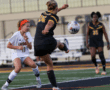 Girls' soccer match action shot with player kicking ball, opponents ready to intercept on a football field.