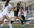 Soccer player in black jersey dribbles past opponent in white, action-packed game moment on the field.