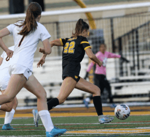 Soccer player in black jersey dribbles past opponent in white, action-packed game moment on the field.