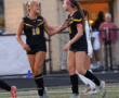 Two female soccer players in black jerseys cheer on the field during a match, showing teamwork and camaraderie.