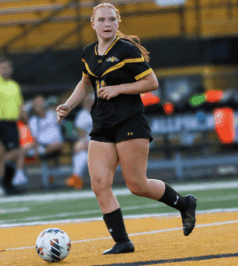 Soccer player in black and yellow uniform dribbling a ball on field during a match.