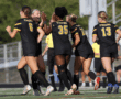 Soccer team celebrates a goal on the field, wearing black and yellow uniforms with Tigers on the back.