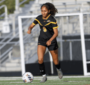 Soccer player in black and yellow uniform dribbling the ball on field during a game.