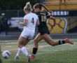 Two female soccer players competing for ball on field, wearing number 4 and 15 jerseys, vibrant action shot.