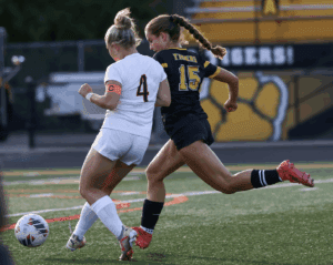 Two female soccer players competing for ball on field, wearing number 4 and 15 jerseys, vibrant action shot.