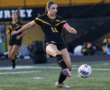 Soccer player in black and yellow jersey kicks ball during a game on green field.