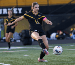 Soccer player in black and yellow jersey kicks ball during a game on green field.