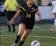 Female soccer player in black jersey dribbles ball on field during match, with referee and opponents in background.