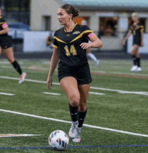 Soccer player in black and yellow uniform dribbling a ball on a field during a match.