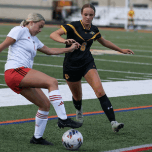 Two female soccer players in action on a field, one in a white and red kit and the other in black and yellow.