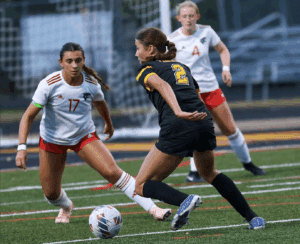 Soccer player in black jersey dribbles past opponents on field during match.