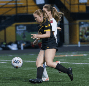 Soccer players in action on the field, one in black and yellow, the other in white, with focus on the ball.