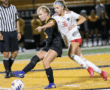 Two female soccer players compete for the ball during a match on a vibrant field.