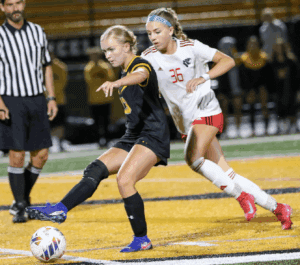 Two female soccer players compete for the ball during a match on a vibrant field.