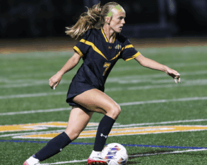 Soccer player in action on the field, wearing black and yellow jersey, dribbling a ball during a night match.