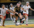 Two soccer teams competing intensely during a night match, players vying for the ball on the field.