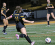 Soccer player in black and yellow uniform kicks ball during a night match on the field.