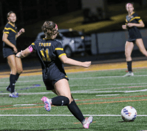 Soccer player in black and yellow uniform kicks ball during a night match on the field.