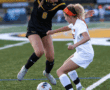 Two female soccer players compete for the ball on a grassy field during a match.