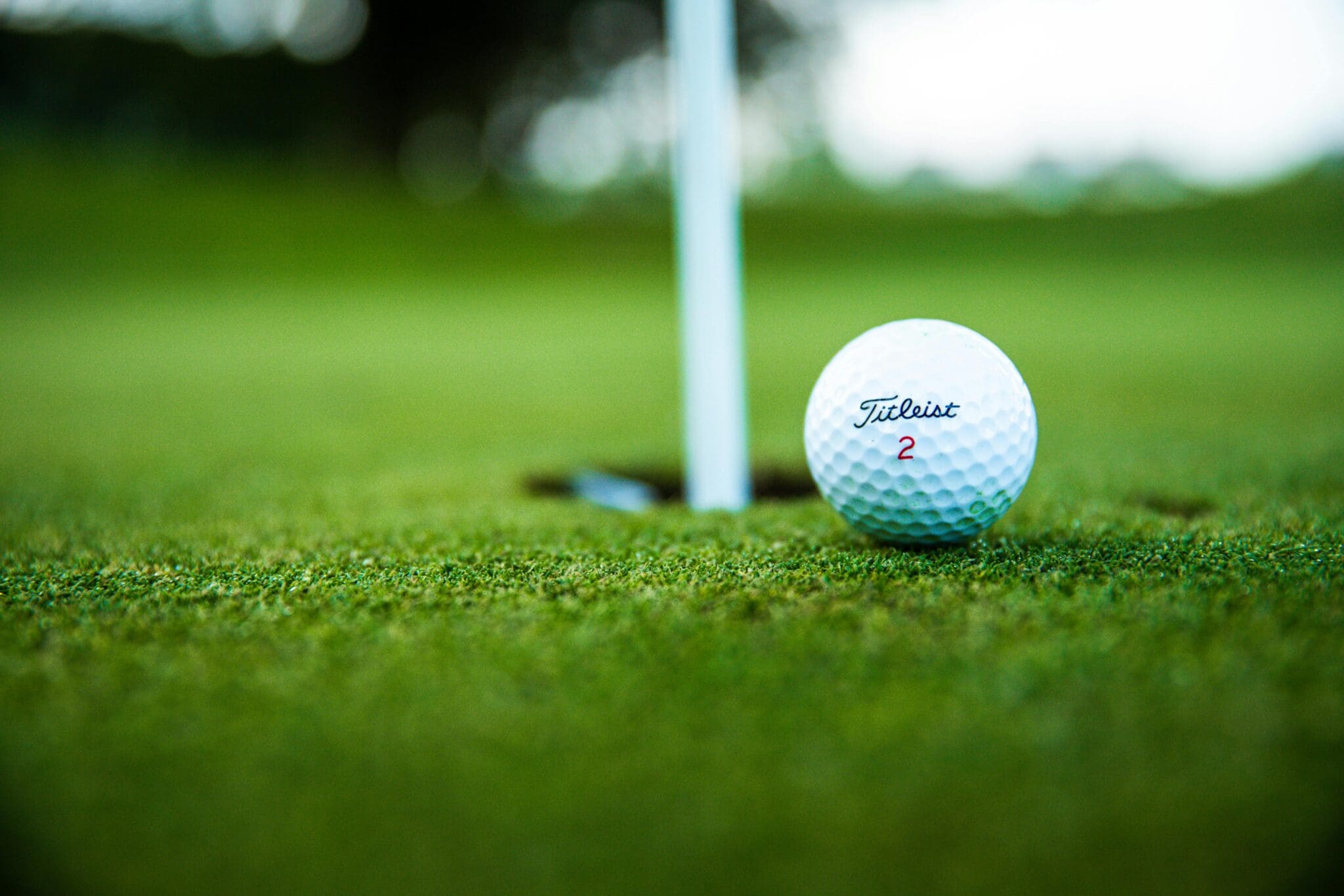 Golf ball near hole on green grass, close-up view of putting scene.