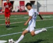 Soccer player in white jersey kicks ball on green field during a game.