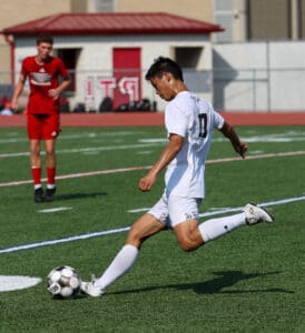 Soccer player in white jersey kicks ball on green field during a game.
