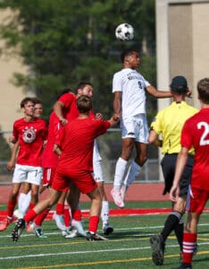 Soccer players compete for a header during a match on a sunny day.