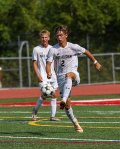 Soccer player in white uniform skillfully controls the ball on a vibrant field during a sunny match day.