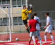 Goalkeeper in yellow jersey catches soccer ball mid-air during a game on a sunny day.