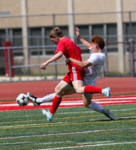 Soccer players in action on the field, one in red dodging a tackle, focusing on the ball during a competitive match.