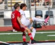 Two soccer players from opposing teams compete for the ball during a match on a sunny day.