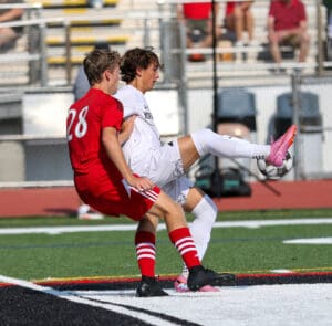 Two soccer players from opposing teams compete for the ball during a match on a sunny day.