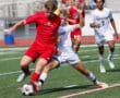 Two soccer players compete fiercely for the ball during an intense match on a sunny day.