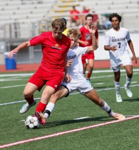 Two soccer players compete fiercely for the ball during an intense match on a sunny day.