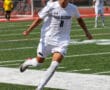 Soccer player in white uniform controls ball on the field during a match.