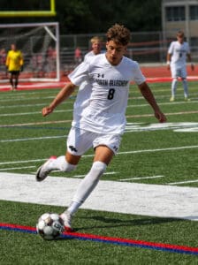 Soccer player in white uniform controls ball on the field during a match.