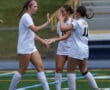 Three female soccer players in white jerseys celebrating on the field with high-fives.