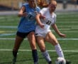 Two female soccer players competing for the ball during a match on a sunny day.