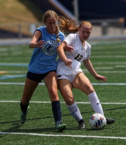 Two female soccer players competing for the ball during a match on a sunny day.
