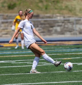 Soccer player in white uniform kicking ball on field during match.