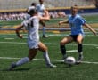 Two female soccer players compete for the ball on an outdoor field during a match.