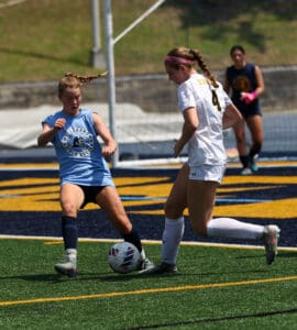 Two female soccer players competing for the ball during a match on a sunny day.